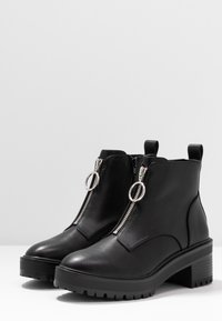 Black leather ankle boots with a chunky heel, side zippers featuring silver hardware, and textured rubber soles.