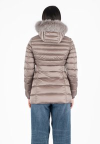Giacca a vento in taupe chiaro con cuciture orizzontali, cappuccio foderato in pelliccia e polsini elasticizzati; abbinata a jeans blu larghi.