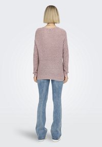 Maglione ampio a maniche lunghe in morbido cotone rosa, con scollatura rotonda e orlo svasato sui lati, abbinato a jeans blu a zampa.