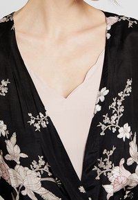 Sort kimono med blomsterbroderi i pink og hvid, med en pink inner top med V-udskæring. Stoffet virker let og glat.