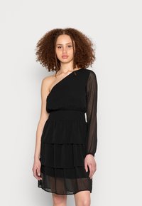 Vestido preto com uma manga longa transparente, cintura franzida e saia com camadas de ruffles. Feito de tecido leve, apresentando um design simples.