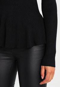 Svart ribbad tröja med utsvängd nederdel och långa ärmar. Tyget är mjukt med en slät yta. Kombinerad med glänsande svarta leggings.