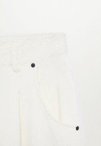 Zone de la taille d'un pantalon en velours côtelé blanc avec passants de ceinture, poche avant incurvée et détails de rivets noirs sur fond blanc.