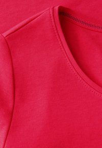 Rød bomulds T-shirt med en tætsiddende rund halsudskæring og glat tekstur. Synlige sømdetaljer langs halsudskæringen og kanten.