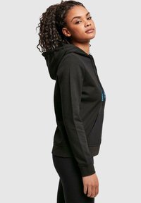 Schwarzer Hoodie mit einer Fronttasche und blauem Textgrafik. Hergestellt aus weichem Stoff, mit einer Kapuze mit Kordelzug und taillierten Ärmeln.