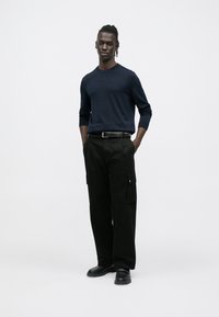 Tumesinine kampsun pikkade varrukatega ja ümmarguse kaelusega, koos mustade küljetaskutega cargo-pükstega. Välimust täiendavad mustad kingad.