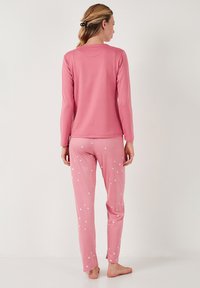 Camisón de pijama rosa de manga larga con cuello redondo, combinado con pantalones rosa a juego que presentan patrones de estrellas blancas, confeccionados en material suave.