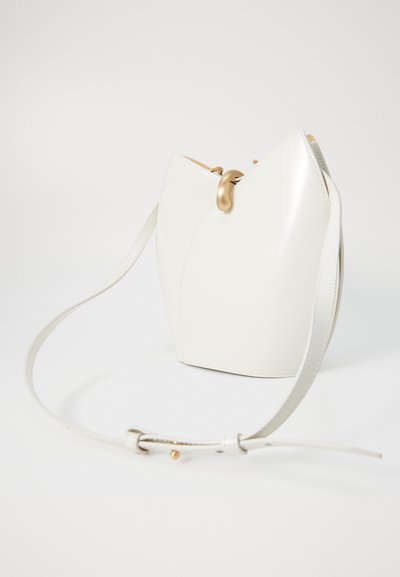 Borsa a secchiello bianca in pelle con design curvo, accessori in metallo dorato e una sottile tracolla regolabile. Texture liscia con dettagli minimi.