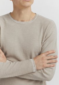 Beige long-sleeve shirt with a textured, ribbed design. Round neckline and contrasting cuffs. Fabric appears lightweight and soft.