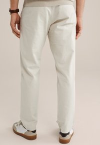 Pantaloni leggeri di colore chiaro con una vestibilità dritta, caratterizzati da una texture liscia e polsini elastici, abbinati a scarpe da ginnastica casual.