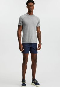 Gray short-sleeve athletic t-shirt and navy shorts. Smooth texture, fitted design. Worn with multicolored sneakers, standing pose.