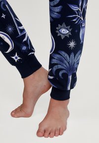 Marineblauwe joggingbroek met een patroon van blauwe en witte hemellichamen, waaronder sterren, manen en potplanten, met elastische boorden bij de enkels.