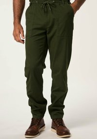 Pantalones cargo verdes con cintura elástica y cordón, que cuentan con bolsillos laterales y un ajuste relajado, combinados con botas marrones con cordones.