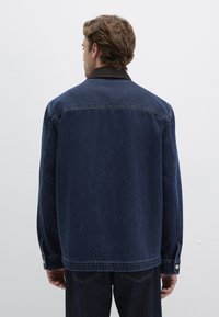 Dunkelblaue Jeansjacke, lockere Passform, mit klassischem Kragen und knöpfbaren Manschetten. Verfügt über kontrastrierende Nähte und eine dezente Textur.