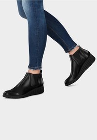 Schwarze Knöchelstiefel aus glattem Leder mit elastischen Seitenpaneelen, einer runden Zehenpartie und einer strukturierten Gummiwedge-Sohle.