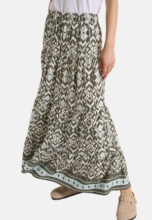 Gonna lunga con fantasia, vita elasticizzata, tessuto a balze e stampa ai bordi, indossata con top bianco e scarpe slip-on beige, in piedi su sfondo bianco.