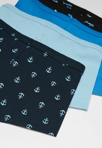 Trois paires de boxers en bleu marine, bleu clair et noir. La paire bleu marine présente un motif d'ancre répété en bleu clair.