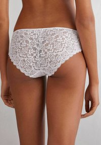Witte kant boyshorts met ingewikkelde bloempatronen, golvende randen en een zachte textuur. Het ontwerp onthult een delicate, semi-doorschijnende uitstraling.
