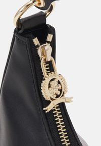 Czarna skórzana torebka z złotymi okuciami. Posiada zamek błyskawiczny z detalem herbu lwa oraz teksturowaną czarną tkaninę. Trójkątny kształt.