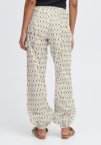 Pantalons en tissu crème léger avec un motif de flèches noires verticales. Dotés d'une taille élastique et d'une coupe décontractée avec des chevilles effilées.