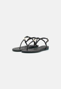 Sorte flate sandaler med teksturert såle, slanke stropper og detaljer i gulltone. Designet med en minimalistisk form og stil.