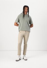 Lys grøn bomulds T-shirt med korte ærmer, parret med beige chinos og grå sneakers med sorte striber. Enkelt, minimalisk design.