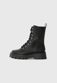 Mustad nahast lahingukinga, millel on paks tald, paeltega ette, külgkäepide ja nahale pressitud DKNY logo pahkluul.