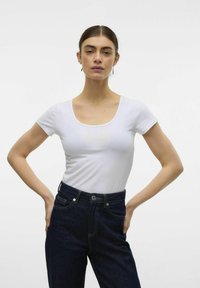 Vit kortärmad T-shirt med rundad halsringning, ihopparad med mörkblå högmidjade jeans med kontrastsömmar och knäppning.
