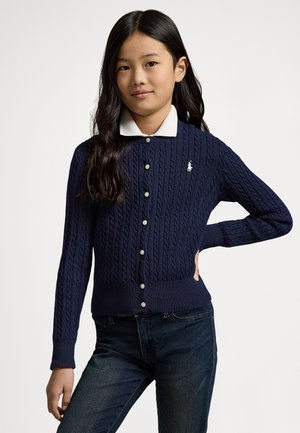 Marineblå kabelstrikket cardigan med hvit krage, med knapper foran og en liten brodert logo på venstre side.