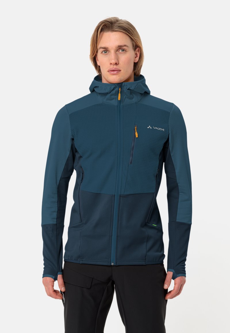 Giacca con cappuccio da uomo, blu scuro, tessuto leggero, pannello frontale trapuntato, tasche con zip, polsini elasticizzati, orlo regolabile, branding minimale.