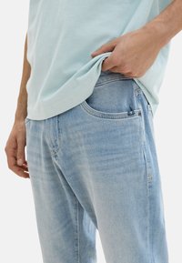Helle blaue Jeans aus Denim mit einem lockeren Schnitt, versehen mit frontalen Taschen und einem dezenten Waschungseffekt, kombiniert mit einem hellblauen T-Shirt.