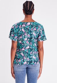 Květinová blůza tmavě zelené barvy, s krátkými volnými rukávy a uvolněným střihem. Různé odstíny růžových květů vytvářejí živý vzor.