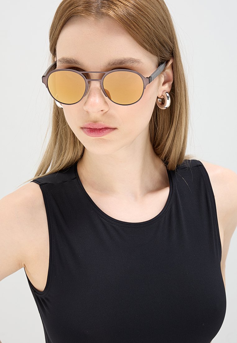 Gafas de sol con lentes redondos de color ámbar y un marco delgado de plástico gris. El diseño es minimalista, sin logotipos ni patrones visibles.