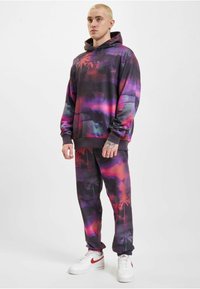 Set di felpa con cappuccio e pantaloni della tuta in un motivo tie-dye nero, viola e rosso. Presenta polsini elasticizzati e vita a contrasto. Sneakers bianche.