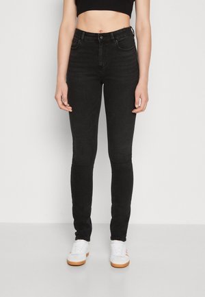 Jeans skinny negros de cintura alta con una textura suave, bolsillos delanteros y un diseño ajustado. Combinados con zapatillas blancas con detalles en naranja.