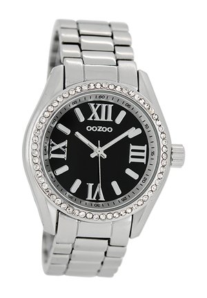 Montre en acier inoxydable argenté avec un cadran noir, des chiffres romains et une lunette ornée de pierres claires. Équipée d'un bracelet en maillons métalliques.