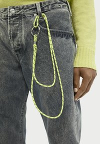Szare dżinsy z denimu z neonowo-żółtym sznurkiem i detalem z liny przymocowanym do srebrnego pierścienia. Teksturowana tkanina z akcentami w formie węzłów.