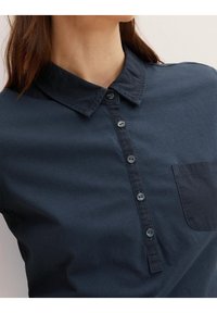 Navy blue collared shirt made of soft fabric, featuring a button-up front, subtle pocket detail, and a smooth, untextured finish.