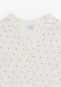 Blusa bianca con scollatura a V, caratterizzata da piccoli motivi quadrati metallici in rame. Realizzata in tessuto leggero con una texture arricciata.