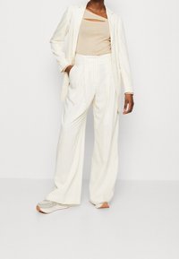 Costume blanc à rayures avec une veste cintrée, un pantalon ample et un débardeur beige. Présente une coupe moderne et une texture de tissu douce.