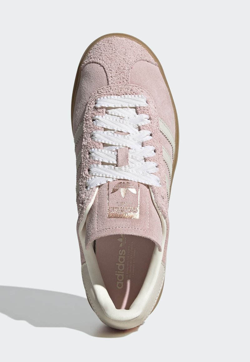 Roze suède sneaker met witte veters, voorzien van een beige rubberen zool en een metalen gouden logo op de tong. Accenten omvatten witte strepen.