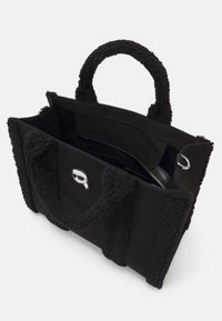 Sac cabas noir avec anses texturées, ouverture supérieure montrant une poche intérieure zippée et petit emblème argenté sur le panneau avant.