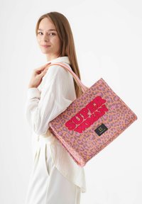Tote bag à imprimé léopard en rose et orange avec le texte "SUPER WOMAN", équipée de poignées robustes et d'une étiquette de marque. Finition en tissu texturé.