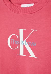 Różowy sweatshirt z żeberkowym dekoltem. Z przodu znajduje się napis "cK" w białym kolorze oraz "This is Love" w jasnoniebieskim, kontrastującym z tłem.