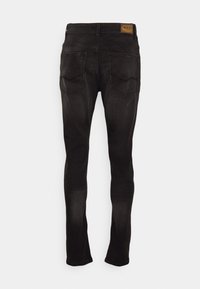 Jean en denim noir avec une coupe slim, arborant un patch logo sur la taille et deux poches arrière avec des coutures en biais. Texture lisse.