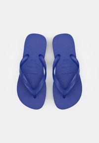 Mėlyni guminiai šlepetės su tekstūruotais pado paviršiais ir V formos dirželiais. „Havaianas“ logotipas integruotas į vieno dirželio dizainą.