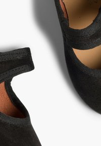 Sorte ruskindssko med elastisk trim omkring anklen, der fremviser en glat overflade og rund form, der afslører et brunt indre.