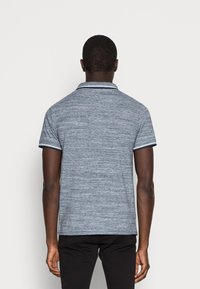 Polo shirt bleu marine avec une texture chinée, doté d'un col classique et d'une bordure contrastante sur les manches, associé à un pantalon noir.