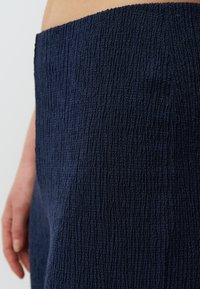 Tessuto in blu navy con una trama a coste, caratterizzato da una vita media e una finitura liscia. Una mano è visibile mentre tiene il tessuto.