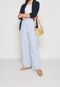 Světle modré kalhoty s širokými nohavicemi, bílé upnuté tričko, námořnický otevřený pletený kardigan a béžové ploché boty. Taška je kulatá s jemnou texturou a měkkým držadlem.